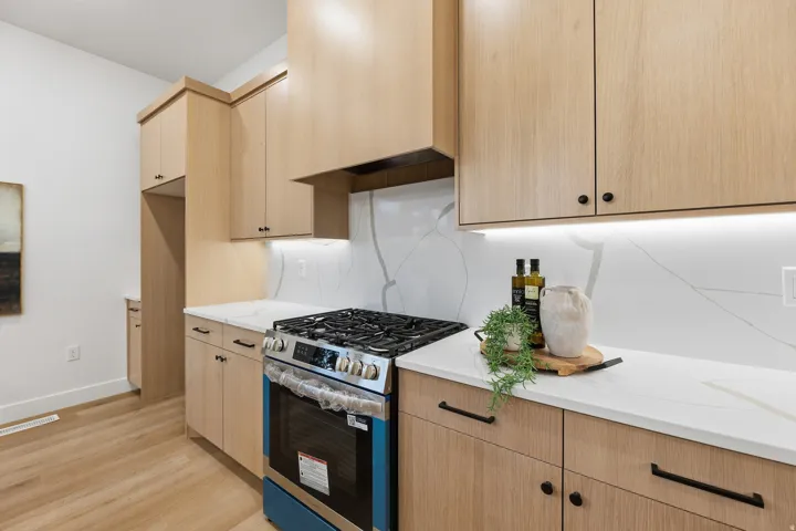 Light wood-finish cabinetry with black hardware, white countertops, a gas range, and a white backsplash with gray veining