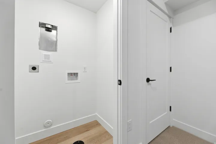 Dedicated laundry area featuring wood-finish flooring, white walls, and a panel door with matte black hardware
