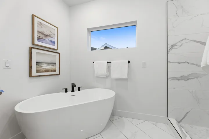 Freestanding soaking tub with matte black fixtures, large format floor tiling, and a glass-enclosed shower with tiled walls