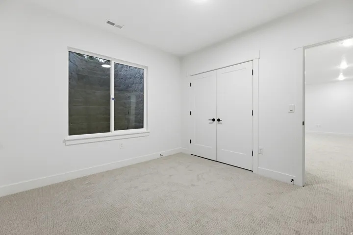 Carpeted room with a large window, double closet doors with matte black hardware, and overhead lighting