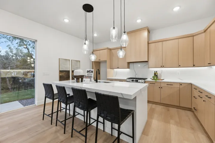 Spacious kitchen featuring light wood-finish cabinetry, a large center island with a white countertop, recessed lighting, and pendant fixtures
