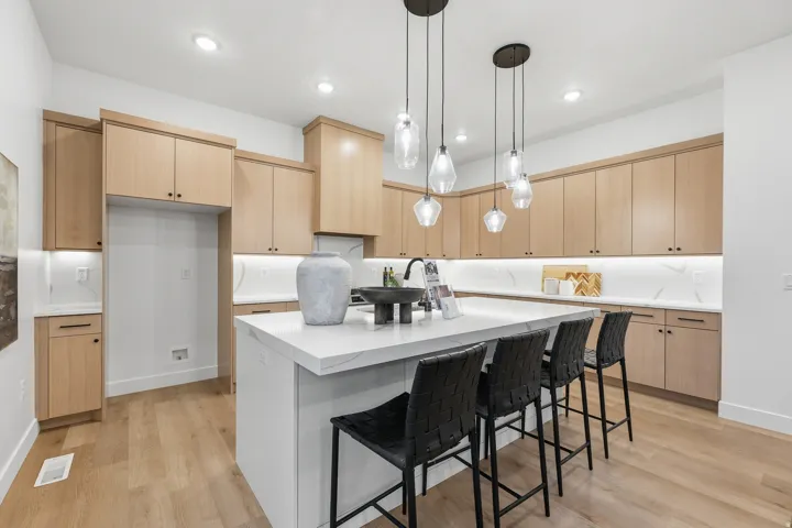 Recessed lighting, wood-finish flooring, light wood cabinetry, white countertops, and contemporary pendant lighting