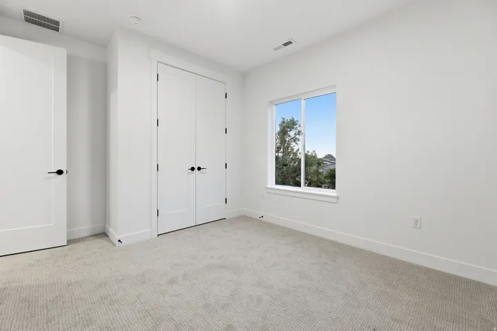 White interior paint, light-toned carpet flooring, a white-framed window, and matte black door hardware