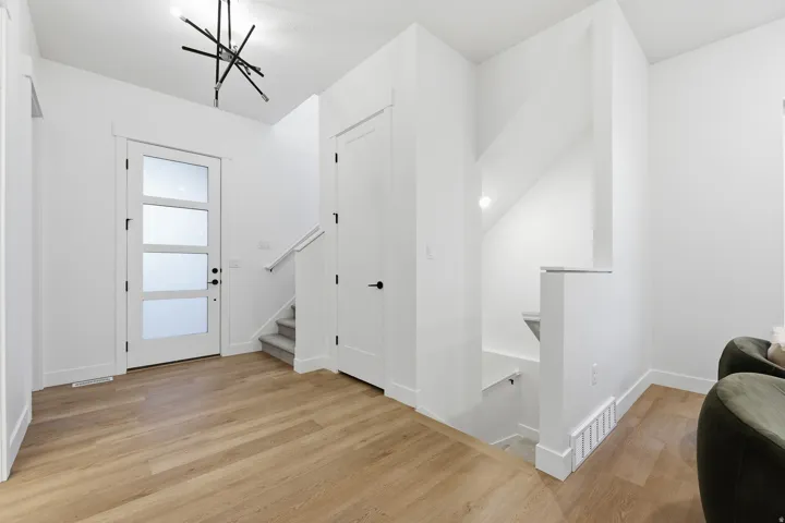 Bright entry space featuring wood-finish flooring, a contemporary black light fixture, and a front door with frosted glass panels