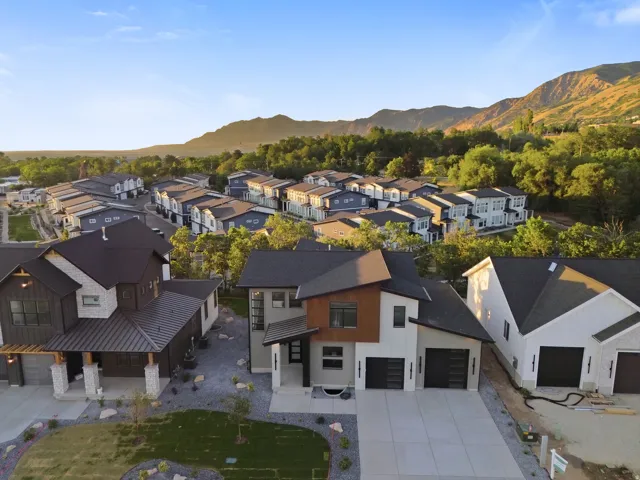 Modern architectural design with a multi-textured exterior, prominent mountain backdrop, concrete driveway, and attached garages