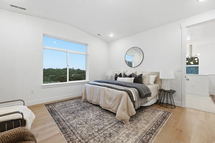 Light wood-finish flooring, white walls, vaulted ceiling with recessed lighting, and a large window with white trim