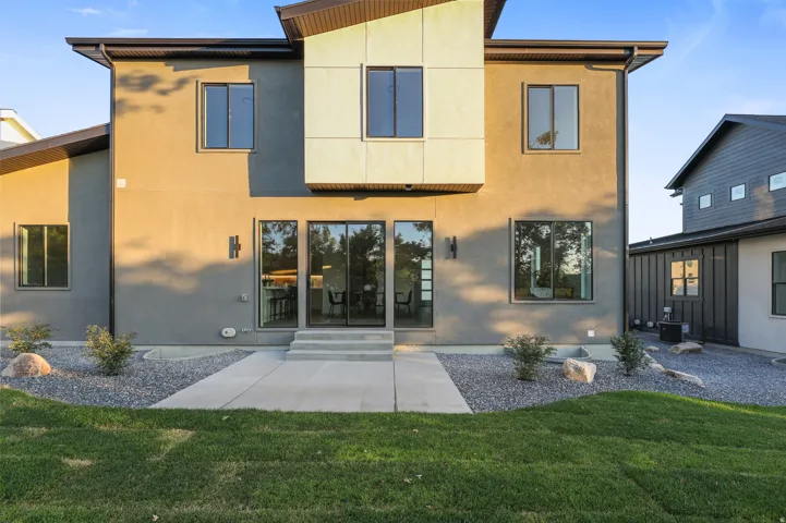Modern stucco exterior with contrasting paneling, large windows, sliding glass doors, concrete patio, and gravel landscaping