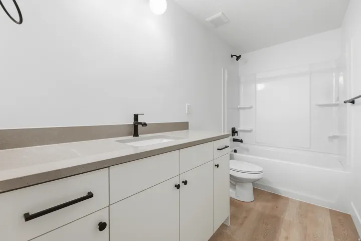White vanity with matte black hardware, light-toned countertop, integrated sink, and wood-finish flooring