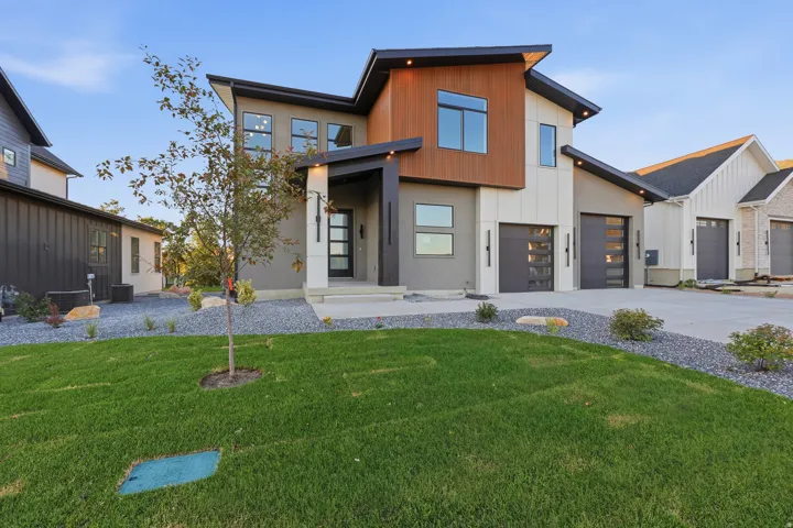 Contemporary exterior with multiple material finishes, a front-facing attached garage, a flat concrete driveway, and a landscaped yard featuring gravel beds and a manicured lawn