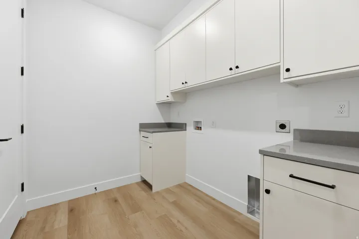 Wood-finish flooring, white cabinetry with black hardware, and grey countertops define this practical space