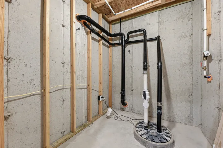 Unfinished space featuring concrete walls, exposed wood framing, a sump pump system, and visible plumbing lines