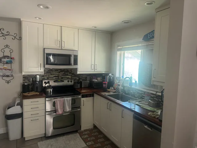 White shaker cabinetry, stainless steel appliances, wood-finish countertops, mosaic tile backsplash, and recessed lighting
