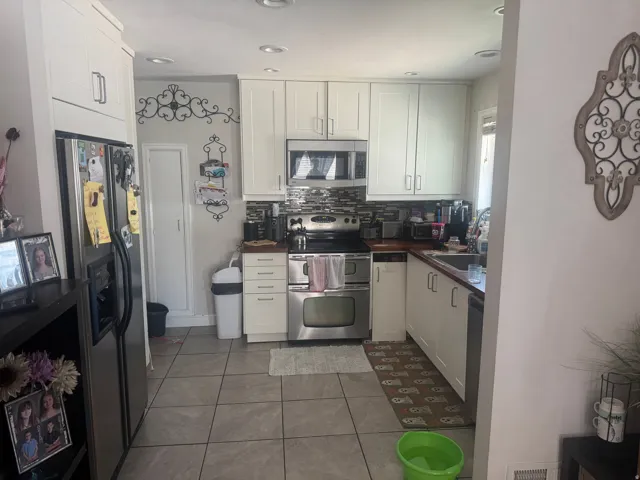 Recessed lighting illuminates a kitchen featuring light-colored cabinetry, stainless steel appliances, and a tiled backsplash