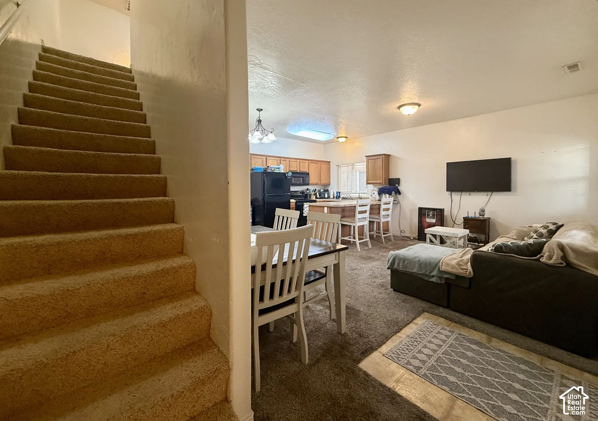 Carpeted staircase, kitchen with wood-finish cabinetry, and an open-concept living area with integrated lighting