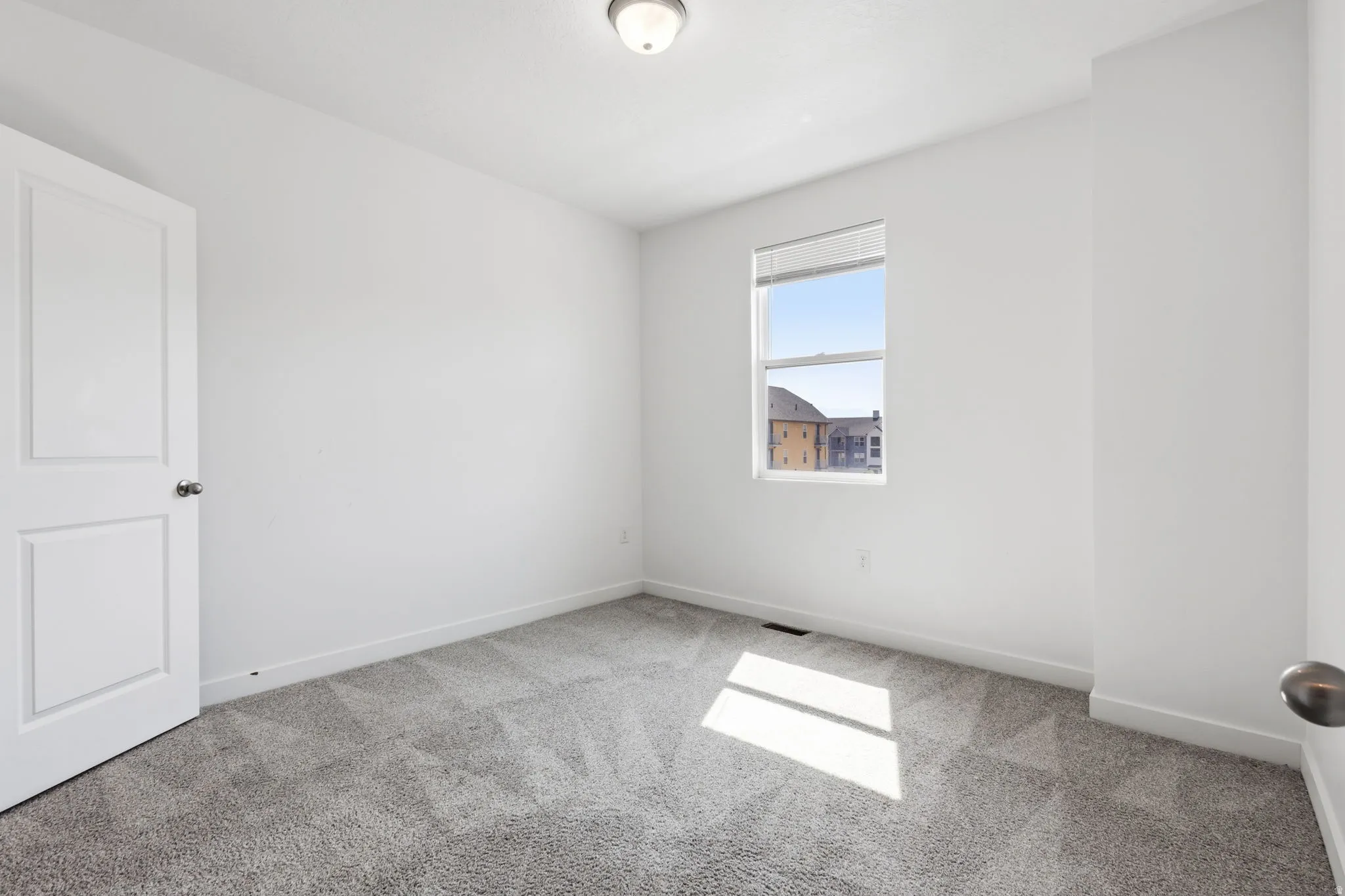 Neutral wall paint, gray patterned carpet, white trim, single window, and flush mount ceiling light
