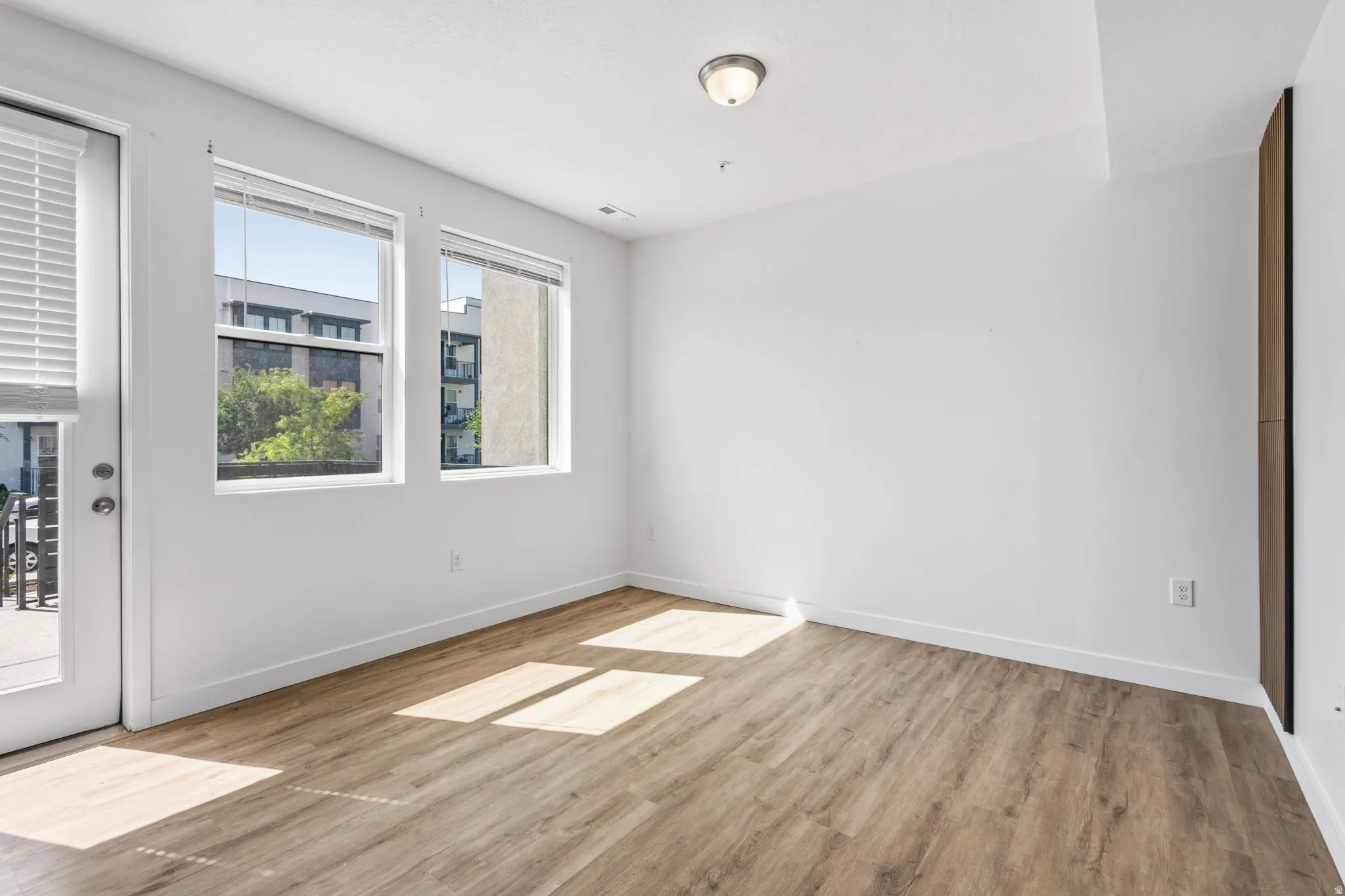 Wood-finish flooring, white walls, two window units, and a glass-paneled door