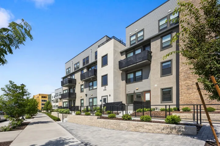Contemporary multi-story building featuring balconies with black railings, horizontal siding, and brick accents
