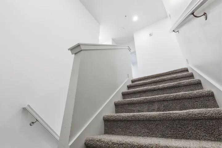 Carpeted staircase with white risers and handrails, featuring recessed lighting
