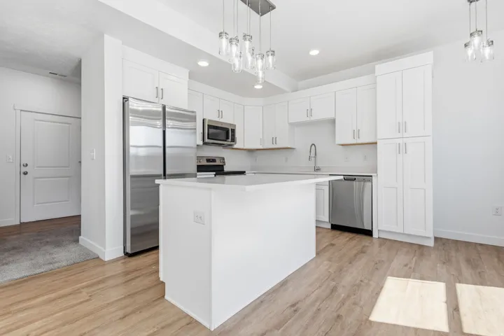 Modern kitchen featuring white shaker cabinetry, stainless steel appliances, a center island with a light-toned countertop, and wood-finish flooring