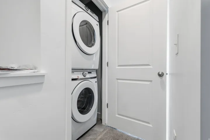 Built-in laundry closet with a stacked washer and dryer unit, white paneled door, and brushed nickel hardware