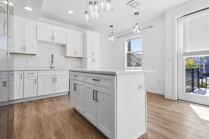 White shaker cabinetry, light-toned countertops, wood-finish flooring, island with integrated storage, and balcony access