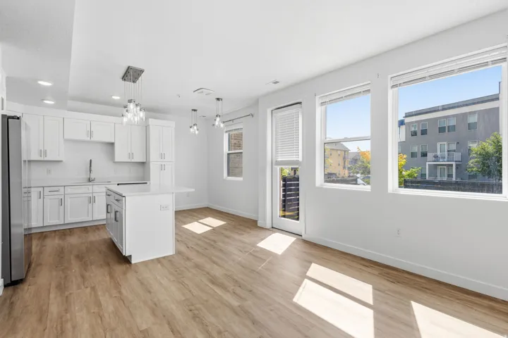 Open-concept living space with wood-finish flooring, a kitchen island with seating, white cabinetry, and stainless steel appliances