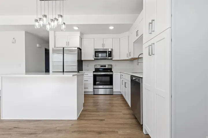 Kitchen featuring a center island, white cabinetry, integrated stainless steel appliances, and wood-finish flooring