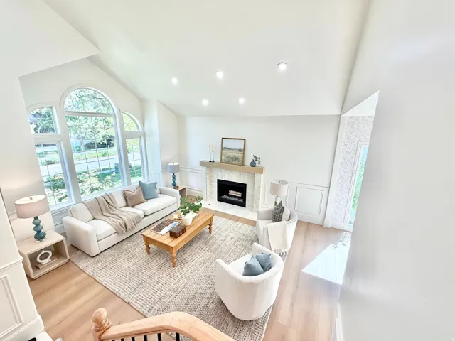 Vaulted ceiling, recessed lighting, large arched windows, fireplace with hearth, and wood-finish flooring