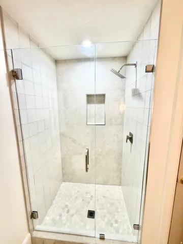 Glass-enclosed shower with pebble-finish flooring, tiled walls, a built-in shower niche, and a rain shower head