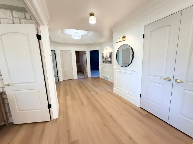 Bright, open hallway featuring warm wood-finish flooring, recessed ceiling lighting, and multiple white six-panel doors