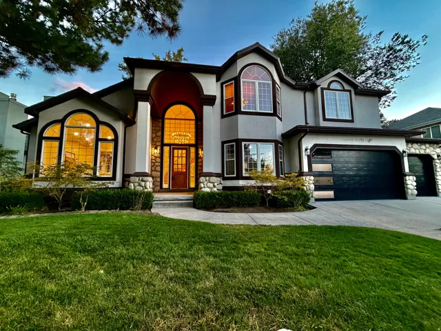 Stucco exterior with stone accents, arched entryway with a wood door, multiple arched windows, two modern garage doors, and a concrete driveway