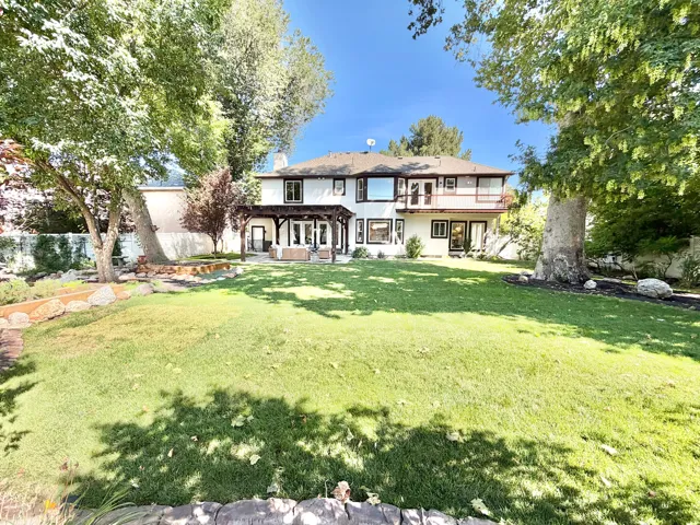Spacious backyard featuring a manicured lawn, established trees, and a pergola-covered patio