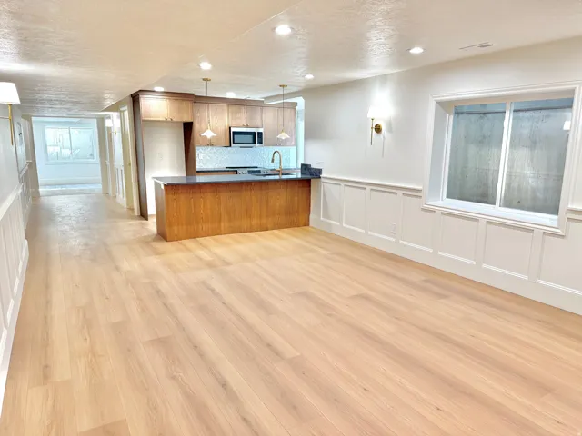 Open concept living area featuring wood-finish flooring, wainscoting, recessed lighting, and a kitchen with wood cabinetry and a dark countertop