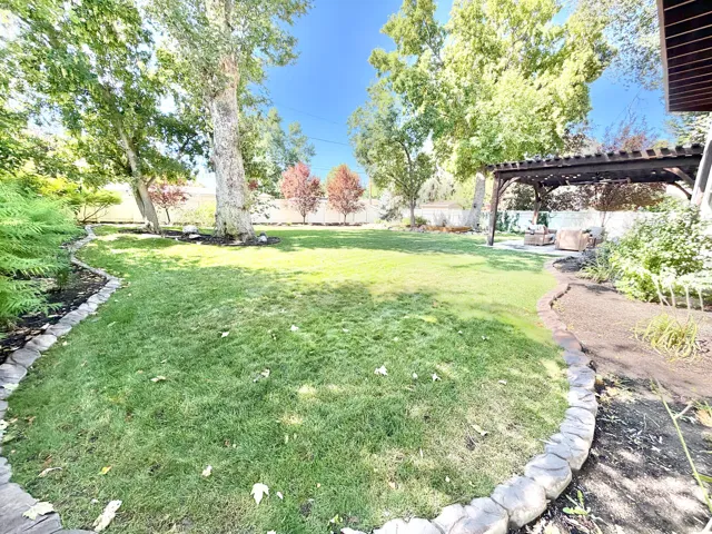 Expansive lawn area, mature trees, wood pergola, stone-edged planting beds, and a paved patio