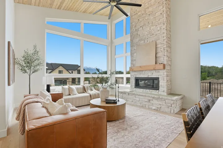 Vaulted ceiling with wood-finish planks, expansive window wall, stone-clad fireplace with wood mantel, and light wood-finish flooring