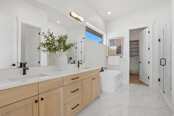 Dual vanity with wood-finish cabinetry, white countertops, large wall mirror, freestanding soaking tub, and a glass-enclosed shower