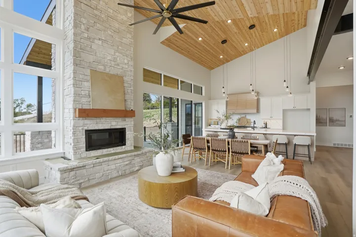 Vaulted wood-paneled ceiling, stone-clad fireplace with wood mantel, large format windows, built-in kitchen cabinetry, and wood-finish flooring