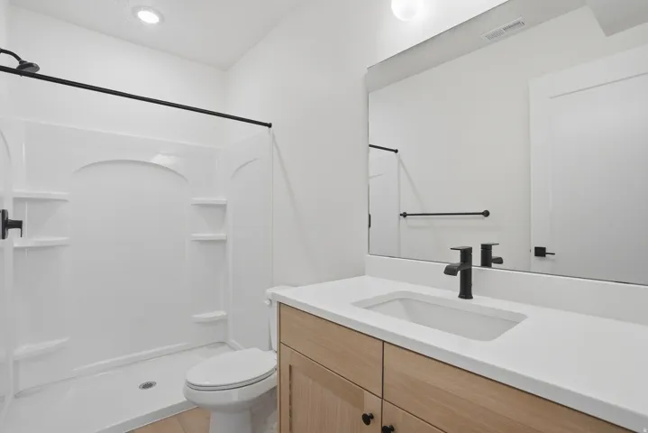 White shower surround with built-in shelving, wood-finish vanity with an integrated sink, and matte black fixtures