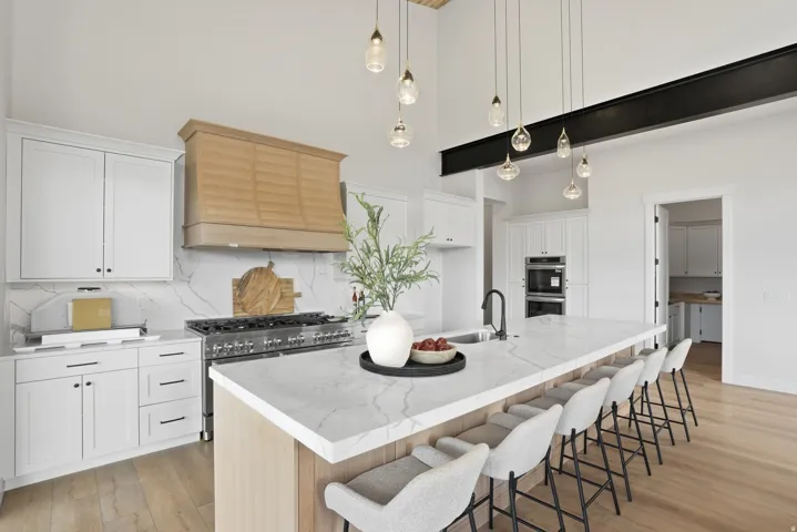 Spacious kitchen featuring an expansive island with seating, high ceilings, wood-finish flooring, a wood-paneled range hood, and a built-in oven and microwave