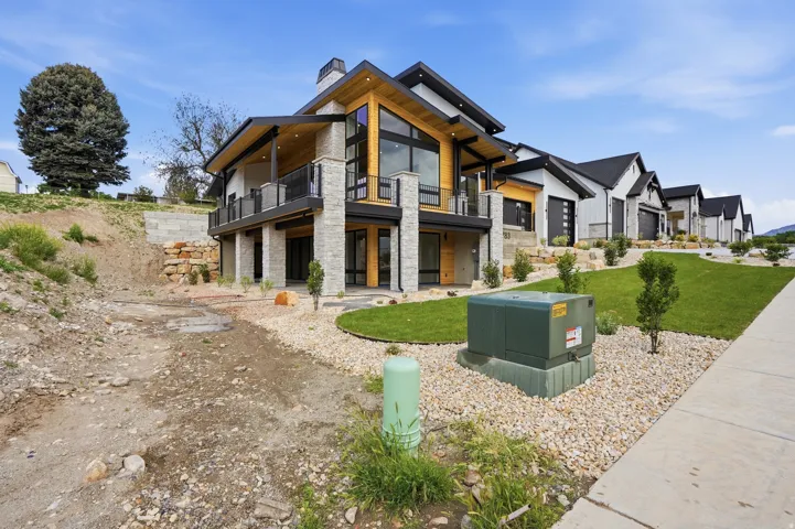 Modern architectural design featuring stone and wood-finish siding, a covered balcony with metal railing, floor-to-ceiling windows, and an attached two-car garage