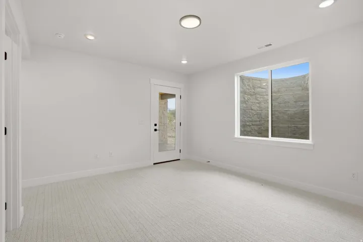 Recessed lighting and a flush-mount fixture illuminate this space, featuring light-colored carpeting, a glass-paneled door, and a window