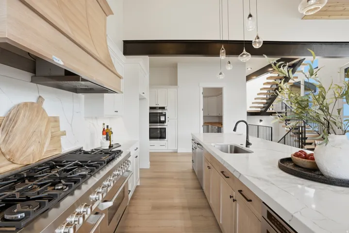 Gourmet kitchen featuring a stainless steel range, wood-finish flooring, white cabinetry, a large kitchen island with an undermount sink, and a staircase with open risers