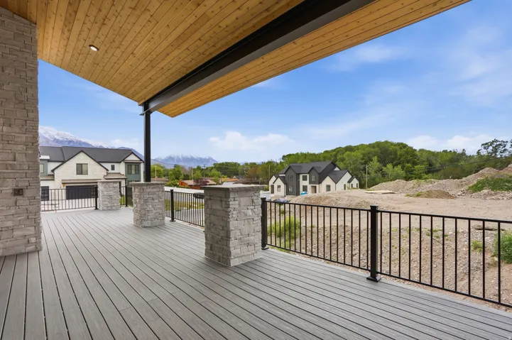 Spacious covered deck featuring composite decking, stacked stone pillars, and a natural wood-finish ceiling