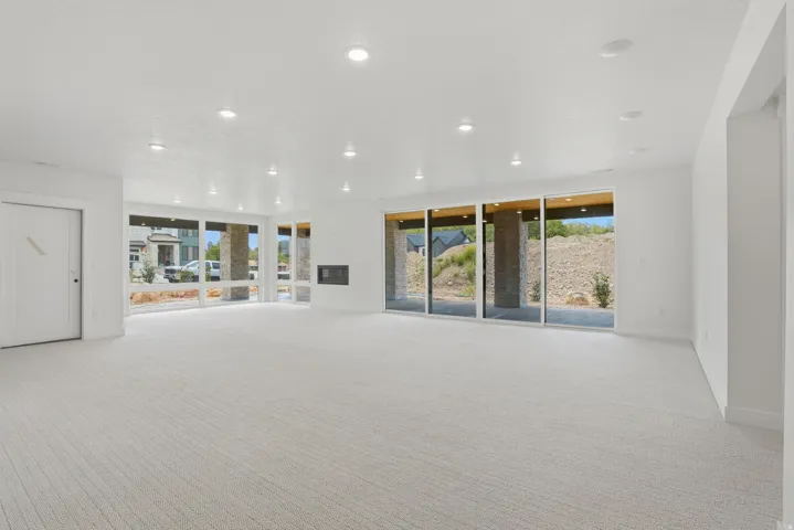 Spacious room featuring light-toned carpeting, recessed ceiling lighting, a built-in fireplace, and expansive windows