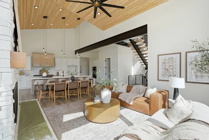 Vaulted wood-finish ceiling with recessed lighting and a ceiling fan, white stacked stone fireplace, open-riser staircase with a black metal railing, wood-finish flooring, and a kitchen featuring white cabinetry and an island