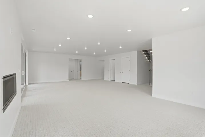 Spacious room featuring light-colored carpeting, recessed ceiling lighting, a built-in fireplace, and multiple white panel doors