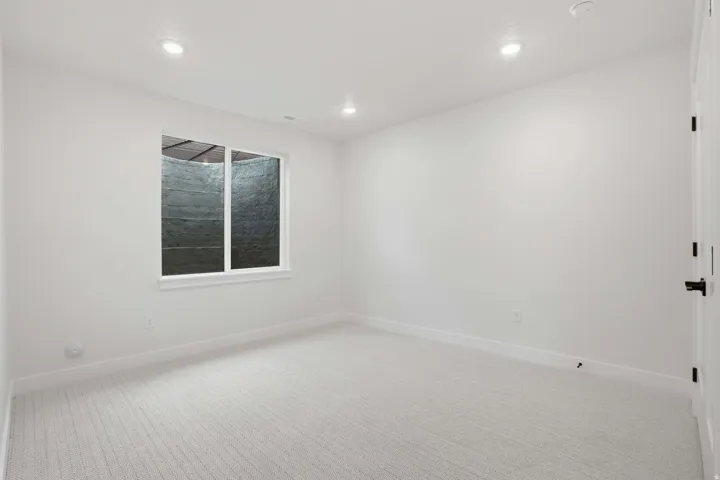 Recessed lighting, new carpet flooring, white walls, white window trim, and a black door handle