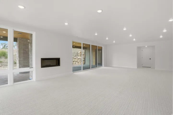 Recessed lighting throughout, wall-mounted linear fireplace, expansive floor-to-ceiling windows, broad sliding glass doors, light-toned carpeting
