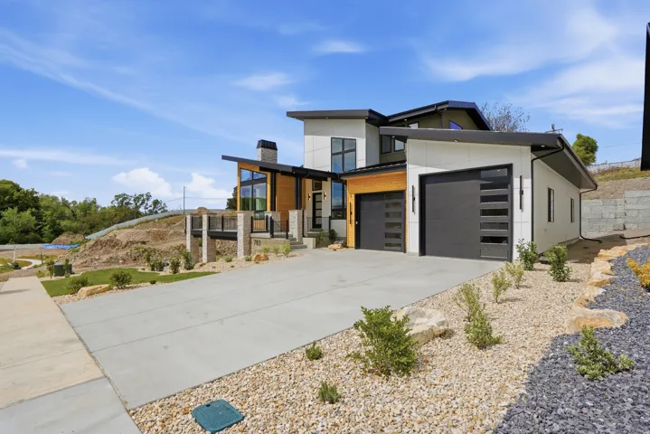 Contemporary exterior with a multi-level design, attached two-car garage, expansive concrete driveway, stone and wood-finish accents, and a landscaped yard with decorative gravel