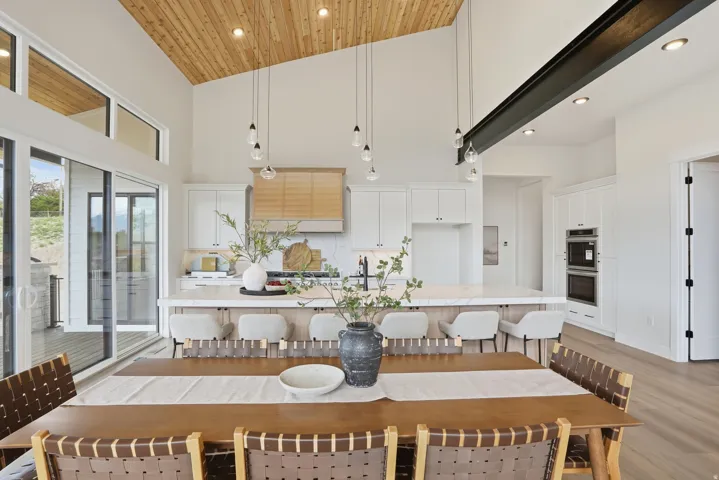 Vaulted wood-finish ceiling, white cabinetry with integrated appliances, kitchen island with seating, pendant lighting, and large sliding glass doors